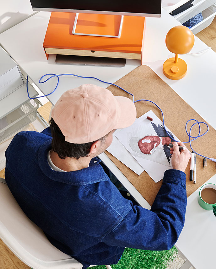 Un espacio de trabajo con un escritorio TROTTEN blanco, regulable en altura, que cuenta con un monitor y una lámpara, además de cuadernos y un teléfono.