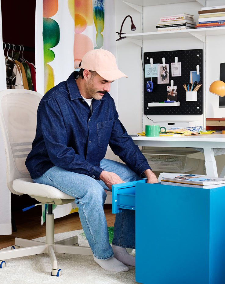 En un espacio de oficina destaca una silla de oficina FLINTAN de color beige, de diseño cómodo, situada junto a un escritorio y unas estanterías con material de oficina.