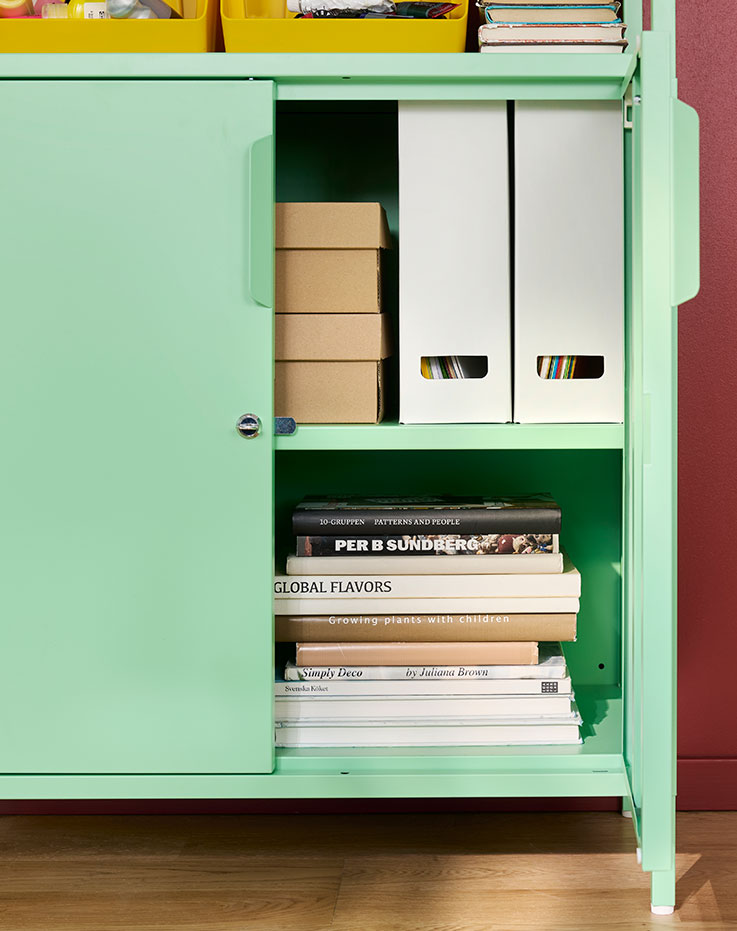 Una oficina en casa con un armario TROTTEN de color verde claro con puertas, en cuyo interior se ven cajas y libros en las estanterías.