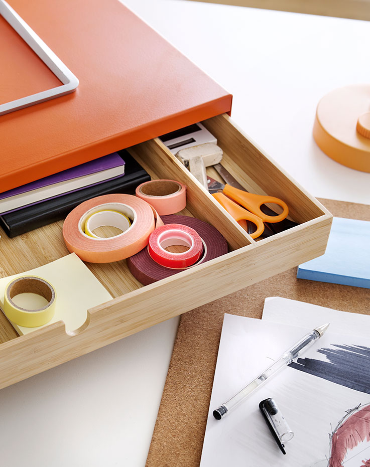 Un primer plano de un soporte para monitor ELLOVEN de color naranja brillante con cajón, en el que se ven artículos de papelería sobre un escritorio.