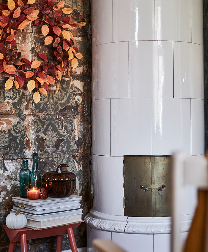 Rincón acogedor de inspiración otoñal con estufa de azulejos blancos, detalles decorativos en tonos cálidos y texturas rústicas que crean un ambiente relajado en el hogar.