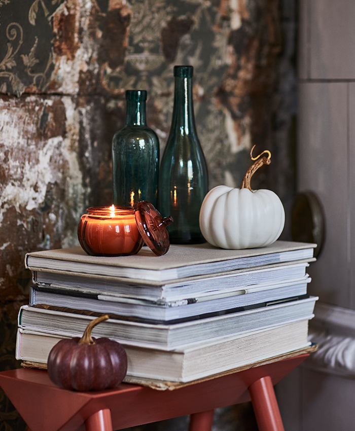 Decoración de temporada sobre una mesa auxiliar con libros, velas y calabazas en tonos suaves, ideal para crear un ambiente cálido y acogedor.