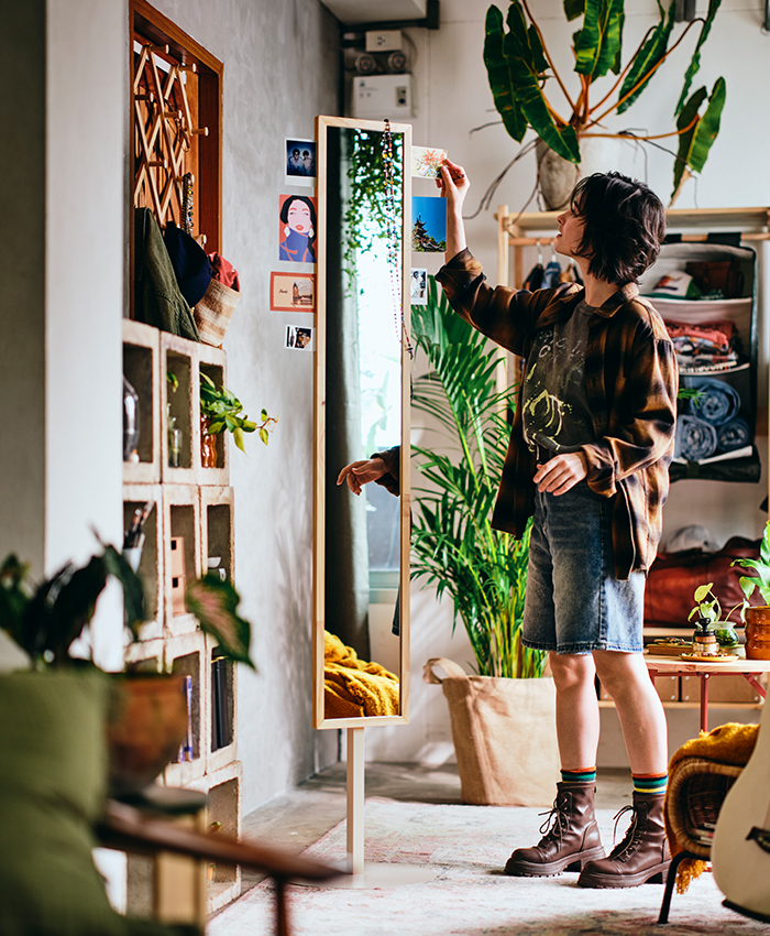 A person places a tall houseplant next to a mirrored wardrobe in a cozy home while decorating and organizing the space.