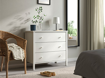 Cozy bedroom with a white dresser, full-length mirror, and wicker chair.
