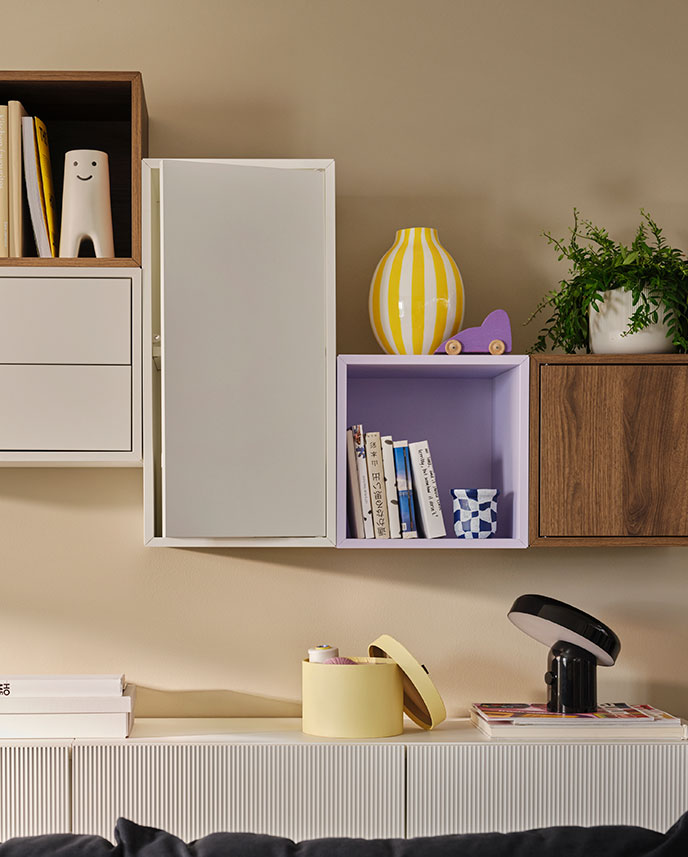 A living room with a white EKET Wall cabinet featuring drawers and shelves, holding books and decorative items.