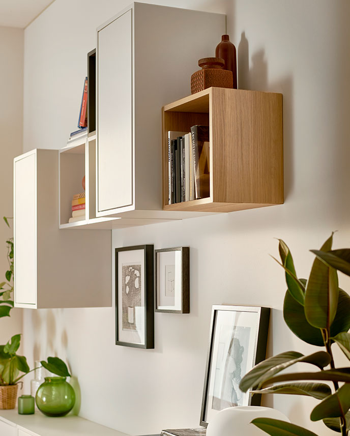 A living room with a white stained Oak effect EKET cabinet holding books and framed art on a light Wall.