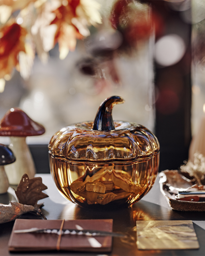 Un cuenco decorativo marrón con forma de calabaza de la marca HÖSTAGILLE, con tapa, lleno de caramelos, junto a dos setas decorativas de HÖSTAGILLE.