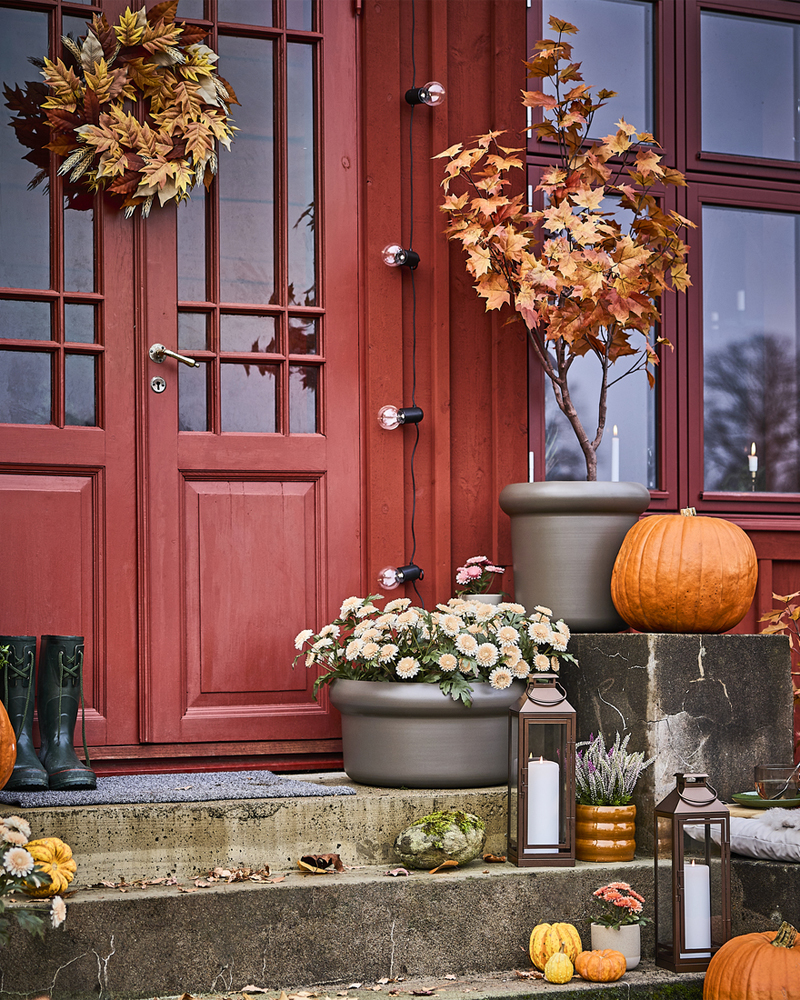 Una escalera exterior con temática otoñal decorada con calabazas y una puerta adornada con una corona artificial de HÖSTAGILLE.