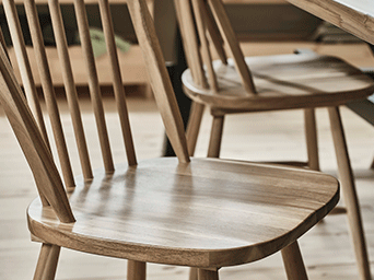 Vista detallada de una silla clásica de madera con respaldo de barrotes, resaltando el acabado suave del asiento y las líneas finas del diseño.