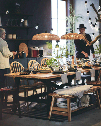 Mesa de comedor alargada de madera con patas negras, bancos a juego con piel sintética y dos grandes lámparas de techo trenzadas.